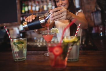 Pretty bachelorette pouring a cocktail drink in the glass at bar