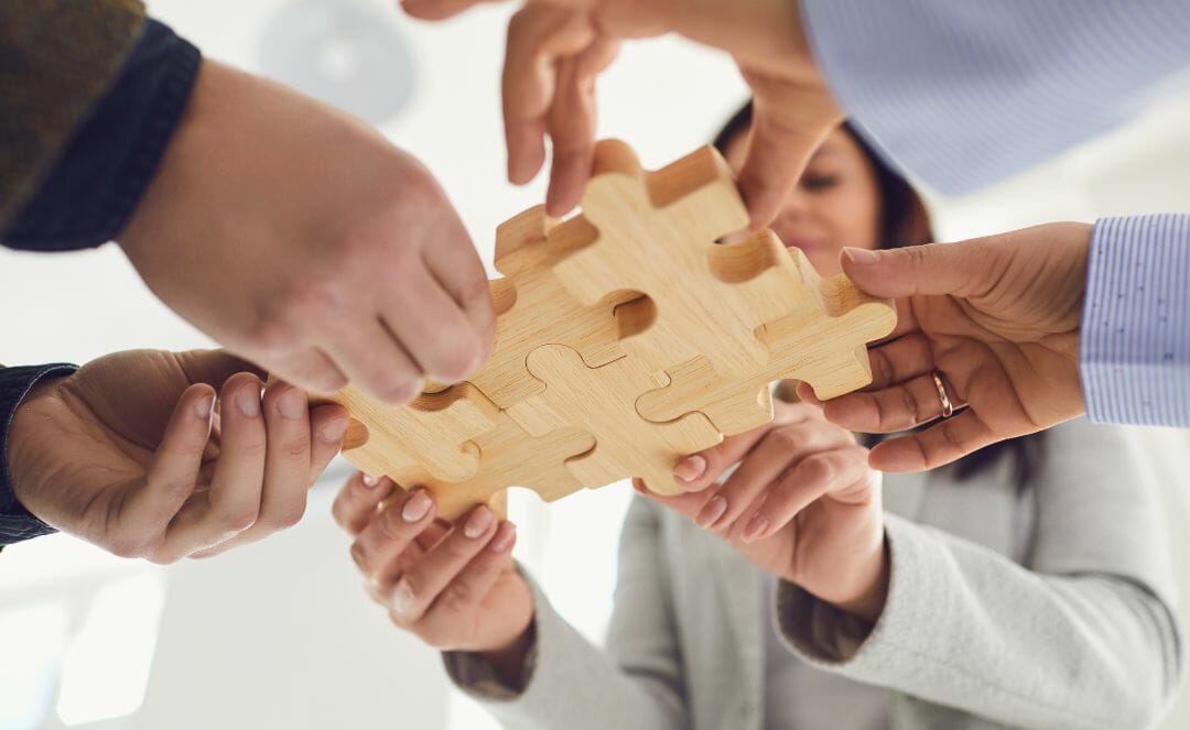 Mensen werken samen om grote houten puzzelstukjes in elkaar te zetten, wat samenwerking in keukenwinkels symboliseert.