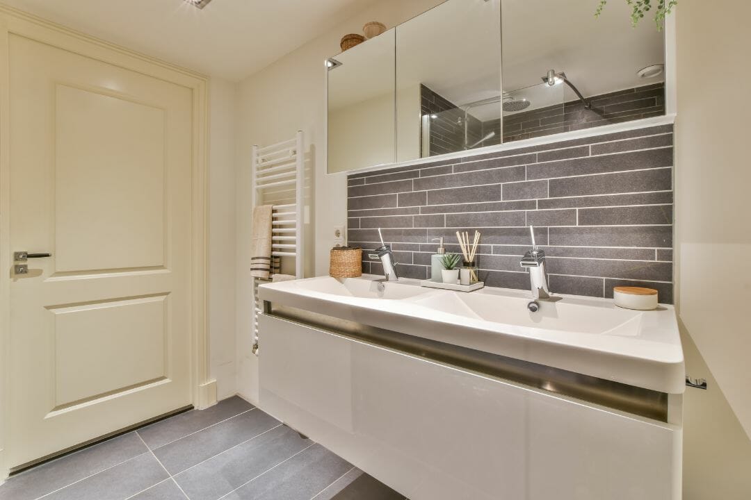 Moderne badkamer met dubbele wastafel, spiegelkasten, handdoekradiator en grijze betegeling. Ideaal voor inspiratie bij badkamerwinkels.