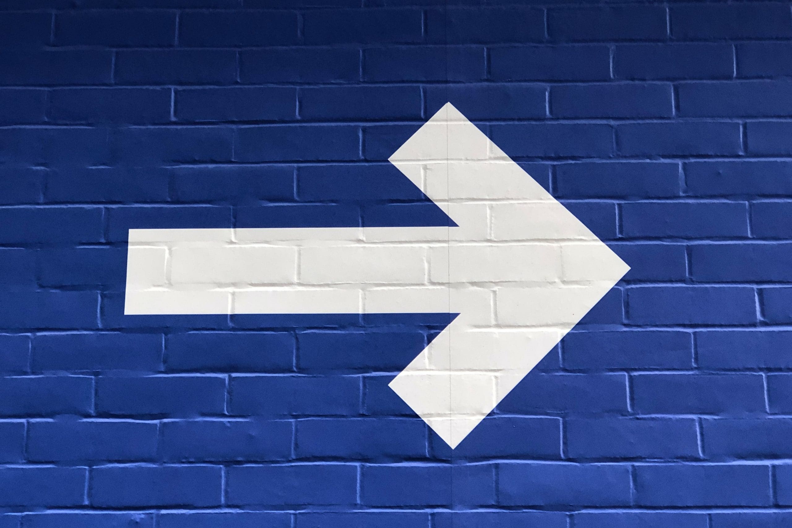 Una gran flecha blanca que apunta a la derecha pintada en la pared de ladrillos azules señala el camino hacia un mejor camino para aquellos que están considerando la transición.