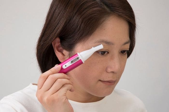 A woman is using a pink electric toothbrush to clean her face.