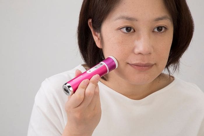 A woman is using a pink electric toothbrush to clean her face.