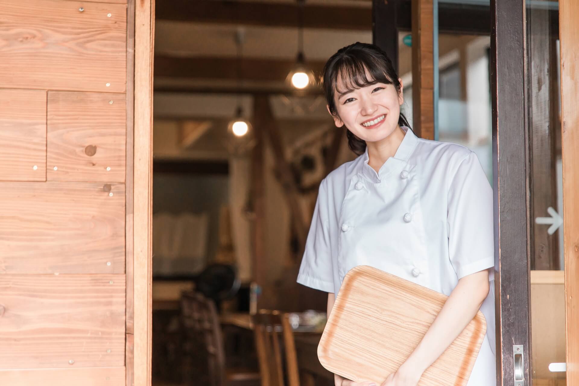 Young asian woman holding wooden cutting board in restaurant.