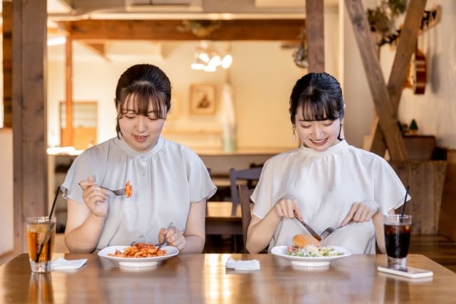 Two asian women sitting at a table eating food.
