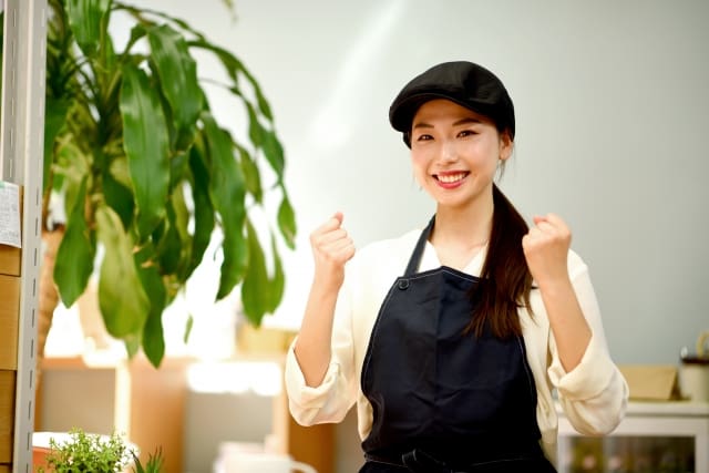 A woman in an apron is standing in front of a plant.