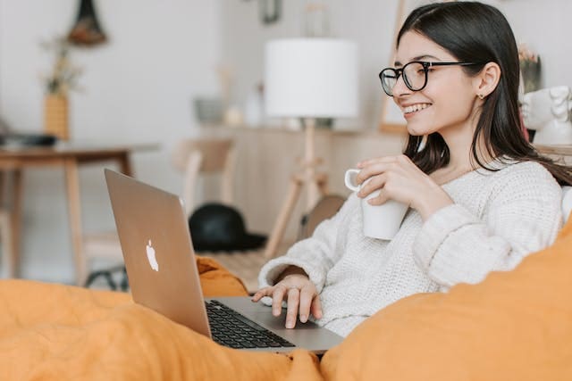 Woman sitting on bed with laptop and coffee.