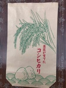 A paper bag with green and red letters advertising the keywords "Gorohei rice (rice grown by farmers with reduced cultivation Koshihikari) 30kg of new rice brown rice (from 10/1 delivery)" and "new rice brown rice".