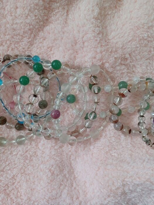 Tegen de achtergrond van zachte lichtroze stof hebben we verschillende op maat gemaakte armbanden op een rij gezet met een combinatie van verschillende gekleurde stenen en doorzichtige kralen.