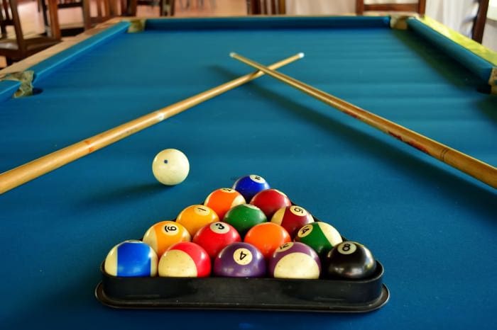 With rows of balls, white cue balls, and two cue sticks crossed on the table, the pool table is perfect for a fun activity during a group trip.