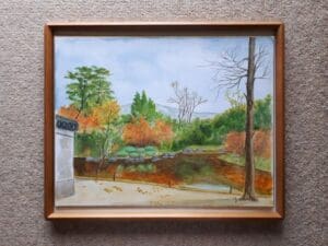 額装された奈良古都の絵画には、色とりどりの木々、水域、左側に部分的に見える建造物のある秋の風景が描かれています。空は青く、地面には葉が散り、その静謐な美しさをこの色紙F6号風景水彩画に捉えています。