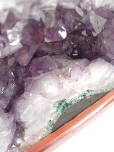 Cận cảnh các cụm tinh thể màu tím và trong suốt với đế khoáng màu xanh lá cây, có thể nhìn thấy một phần trên khay gỗ, giống như mái vòm thạch anh tím.