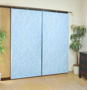 Ang kuwarto ay may maliwanag na kulay na sahig na gawa sa kahoy at dalawang light blue sliding door na may pattern ng puno ng ubas. Sa kanan ng pinto ay isang berdeng palayok na halaman, at sa sulok ay may isang madilim na kahoy na kabinete, na may kurtina na nagse-save ng kuryente na higit na nagdaragdag ng kahusayan sa enerhiya.