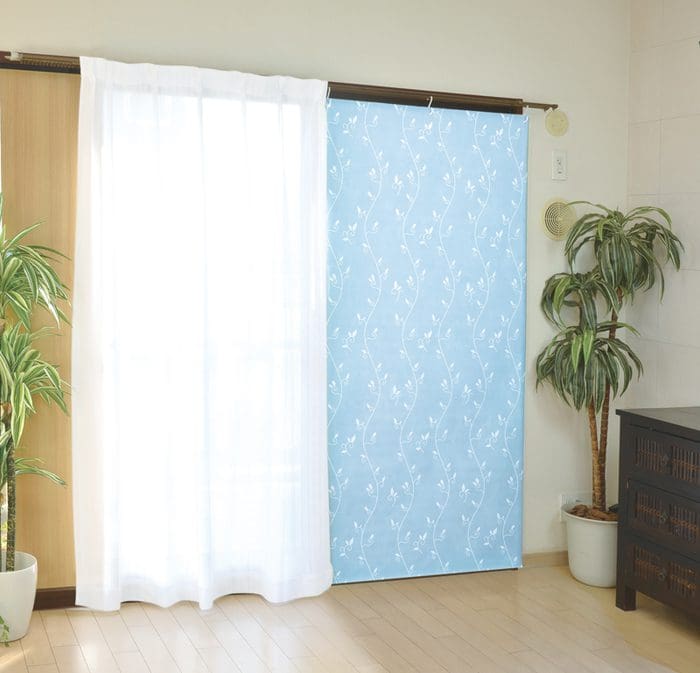 引き戸のある部屋。左側は白い薄手のカーテンで部分的に覆われ、右側は青い模様の遮光カーテンで覆われ、両側に鉢植えの植物が 2 つ置かれています。隅には暗い色のチェストが置かれています。