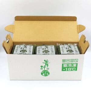 在打开的纸板箱内，有三个绿色和白色的包装，上面用日文字母和符号写着“在 -18°C 下储存”的字样。 包装上标有“Aojiru Hyaku”以炫耀其高品质。