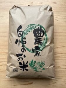A brown paper bag containing 10 kg of fresh white rice with green and black Japanese written on the front is placed on a tree.