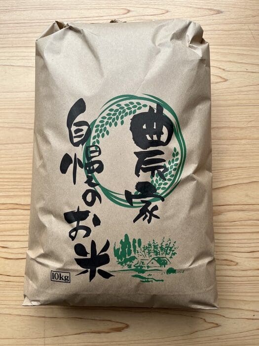 A brown paper bag containing 10 kg of fresh white rice with green and black Japanese written on the front is placed on a tree.