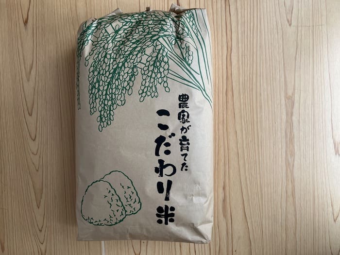 A brown paper bag of fresh white rice with an illustration of green rice and Japanese characters is placed on a tree.