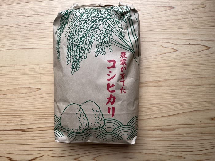 A paper bag of fresh white rice with green illustrations and Japanese characters and the inscription "Reiwa 6" is placed on a wooden surface.