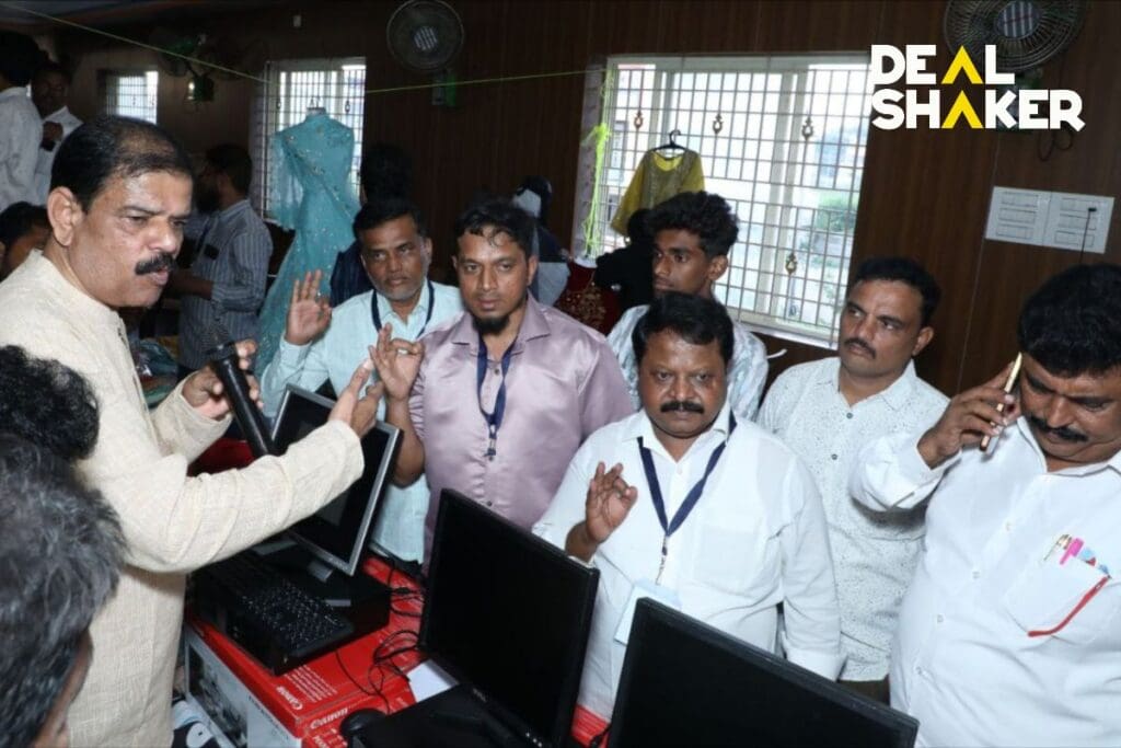 A man talks to a group of men standing around a computer in a room during an IMA event. Several men raised their hands to show interest in the next DealShaker expo to be presented.
