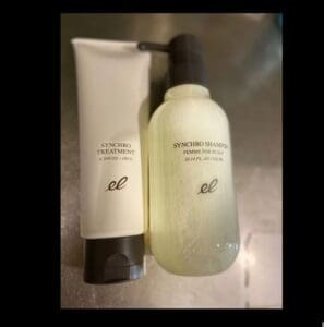 Dalawang mga produkto ng pag-aalaga ng buhok: isang tubo na may label na "Synchro Treatment" at isang bote ng bomba na may label na "Synchro Shampoo Femme for Scalp". Parehong nagtatampok ng isang minimalist na disenyo mula sa tatak ng ELECTRON.