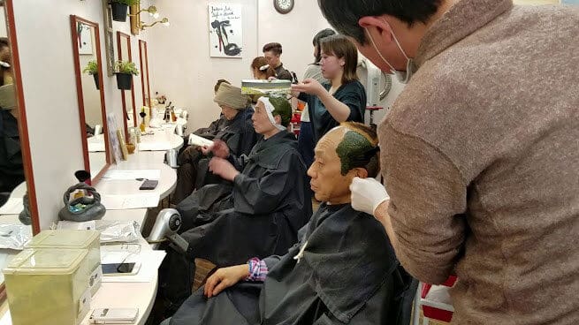 Mga taong nakaupo sa mga upuan sa salon at nasisiyahan sa mga paggamot sa buhok. Maingat na inilalapat ng estilista ang produkto ng henna sa buhok para sa isang marangya at natural na tapusin.