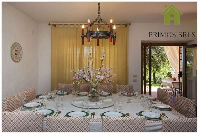 We have a restaurant with a large round table that can accommodate up to 14 people. It features a floral centerpiece and a patterned chair, with a chandelier hanging above. Opening the door leads to the garden outside, perfect for enjoying during the long weekend.