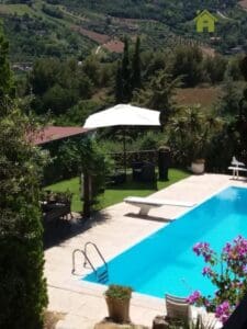 The tranquil outdoor pool area with diving board is surrounded by lush greenery and background hills, providing the perfect getaway at the end of the long week. Parasols can be installed to provide shade near the seats, creating a relaxing space for up to 14 people.