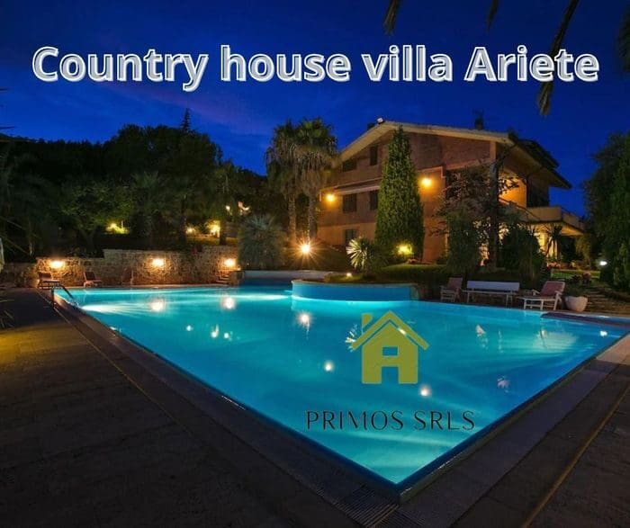 A tranquil night view of the villa awaits, and in the foreground there is a lit-up pool, perfect for a long weekend. Surrounded by trees and illuminated landscapes, this exquisite retreat can accommodate up to 14 people and offers an unforgettable vacation.