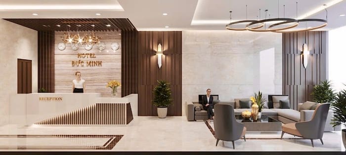 The modern lobby of the Anivia Tamdao Hotel has a front desk on the left and staff behind it. On the right is a seating area with sofas and tables, perfect for admiring the decorative lighting overhead before returning to the deluxe room.