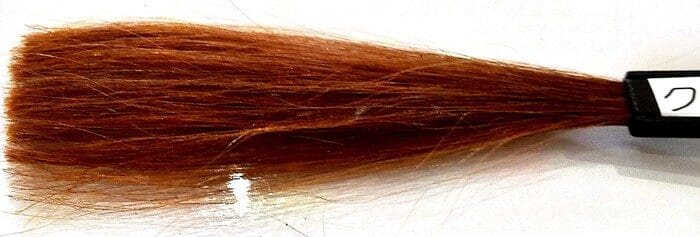 Ang isang sample ng mapula-pula-kayumanggi henna hair dye ay nakasalalay sa isang brush na may label sa sulok.