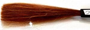 Ang isang sample ng mapula-pula-kayumanggi henna hair dye ay nakasalalay sa isang brush na may label sa sulok.