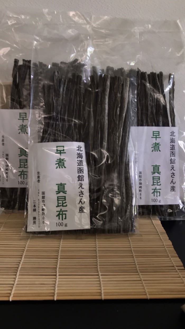 Bags of dried kelp from Eyama, Hokkaido, are arranged upright on bamboo mats and labeled with Japanese labels indicating the exquisite varieties of early-boiled kelp.