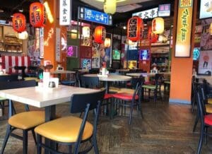 Colorful lanterns, signs, and decorations make the store bright with a Japan theme. Tables and chairs are neatly arranged, and condiments are also placed.