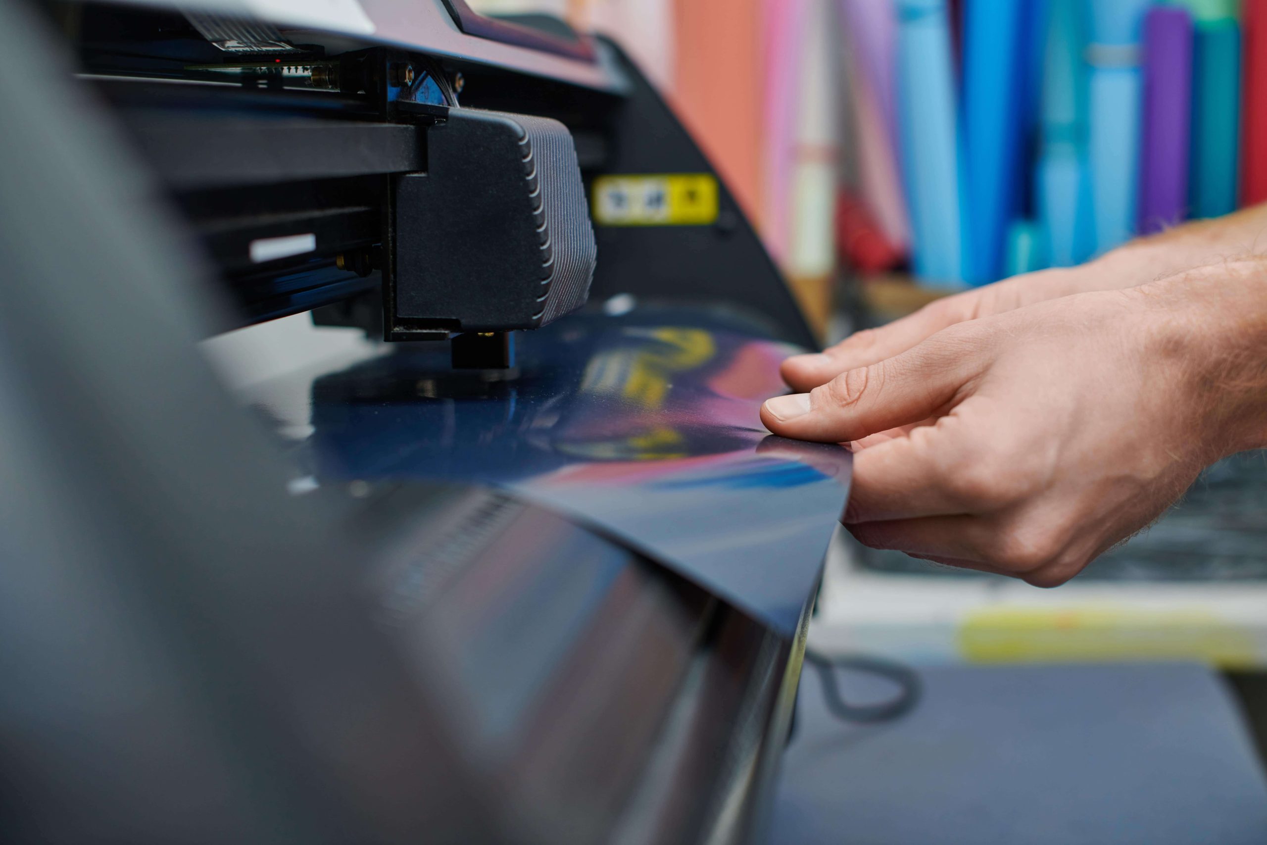 Manos de un operario colocando una lámina de vinilo en un plotter de corte para rotulación.