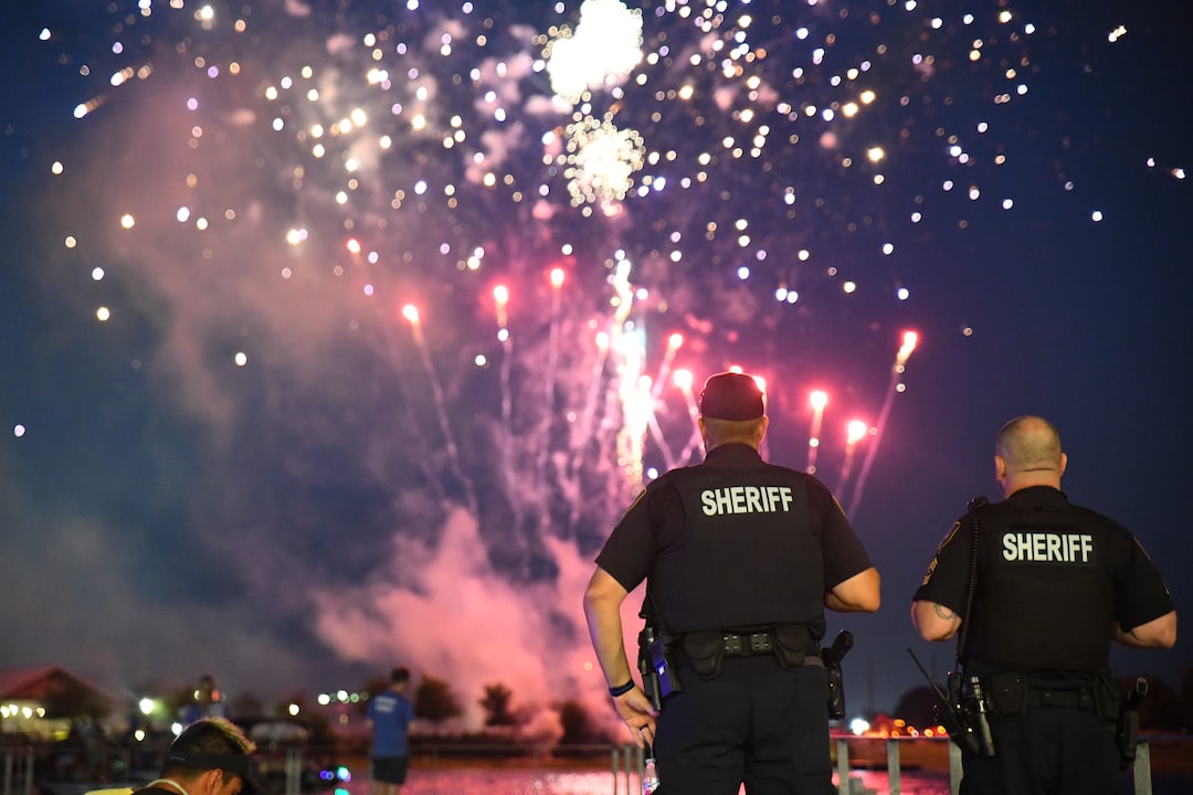 Two police officers watch fireworks over a lake.