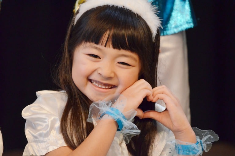 顔の横でハートのポーズをする少女